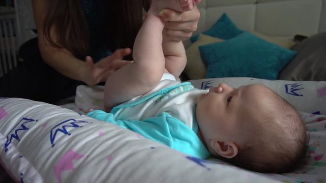 Mom is changing diaper for the baby. A small child is changed a diaper at home on the bed. The child lies in a special cocoon, sometimes capricious. A woman greases the child's ass with powder.