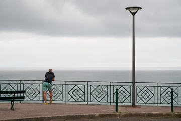 single man back view on fence front of atlantic ocean in city Biarritz Basque Country France