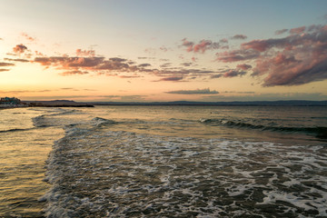 Sea surface with blue water waves under yellow and purple sunset sky.