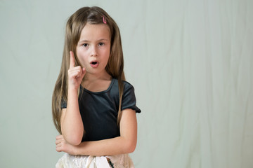 Close-up portrait of happy smiling little girl with long hair holding her finger up having an idea.