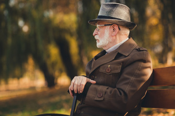 Profile photo of retired old white hair gloomy grandpa street central park sit bench hold walk cane...
