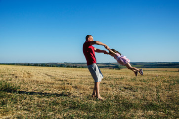 Loving father circles his little daughter against the blue sky. Dad and daughter play merrily in the meadow. Happy parents and children. Walking father and little daughter. Father and daughter. Father