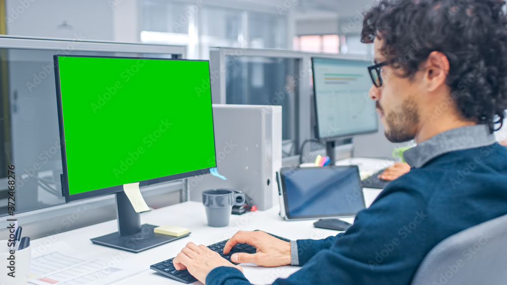 Poster Young Handsome Manager with Curly Hair Works on a Desktop Computer with Green Screen Mock Up. Diverse and Motivated Business People Work on Computers in Modern Open Office.