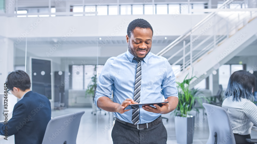 Poster handsome young black manager in a shirt walking pass his business colleagues with a tablet and super