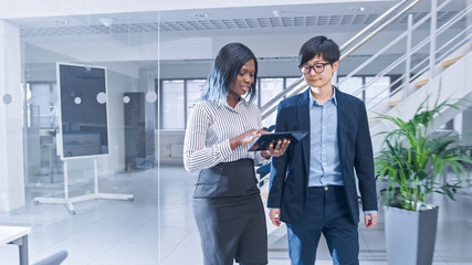 Couple of Young Male and Female Colleagues Walk in the Office Holding a Tablet Computer and Discuss...