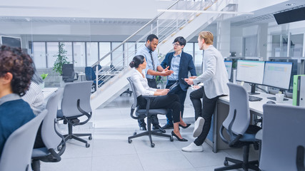 Diverse Multinational Team of Business Managers and Specialists Chat and Discuss Graphs on Paper and Tablet Computer. Young and Motivated Business People in Modern Open Office.