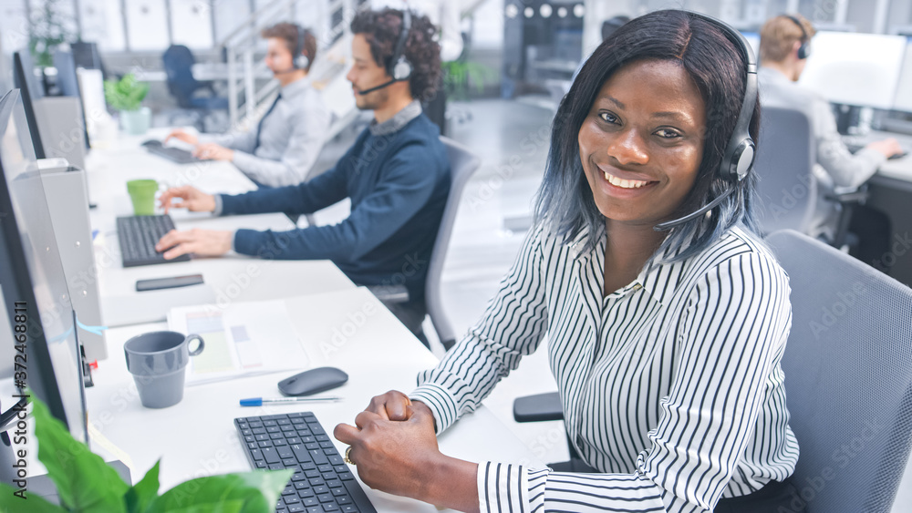 Poster beautiful young female customer service operator smiling for a portrait at a busy modern call center