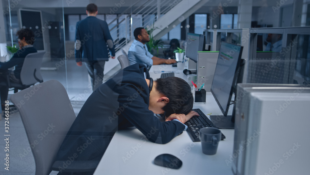 Poster Young Japanese Manager is Tired at his Work Place with Desktop Computer and Falls Asleep. Diverse Multi-ethnic Business People Work on Computers in Modern Open Office.