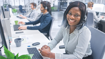 Beautiful Young Female Customer Service Operator Smiling for a Portrait at a Busy Modern Call...