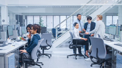 Diverse Multinational Team of Business Managers and Specialists Chat and Discuss Graphs on Paper and Tablet Computer. Young and Motivated Business People in Modern Open Office.