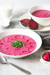 Beetroot gazpacho soup, refreshing summer vegan soup served on a white table with radishes, herbs, sour cream and ice 