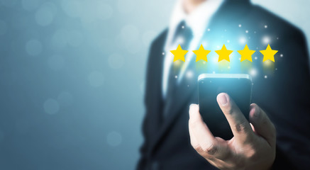 Businessman hand holding smart phone with icon five star symbol to increase rating of company...