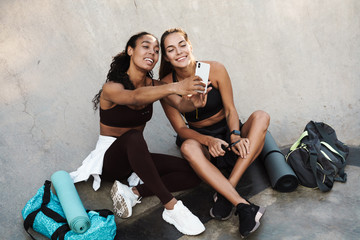 Photo of smiling multinational sportswomen taking selfie on mobile phone