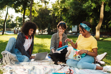 Image of multinational women playing puppy while doing homework in park