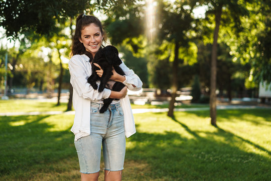 Image of happy woman smiling while posing with puppy in summer park