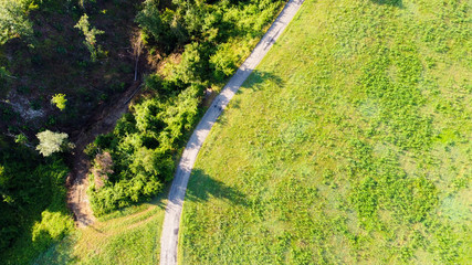 Vista aerea dal drone di una strada di campagna in mezzo a campi e prati con ombre di alberi