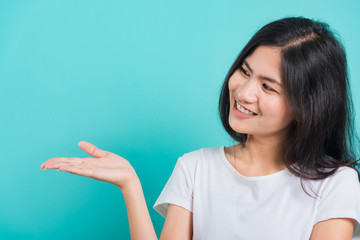 Portrait Asian beautiful young woman standing wear t-shirt, She showing hand to presenting product and looking to product, shoot photo in a studio on blue background, There was copy space