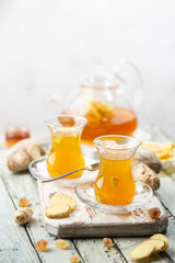 Ginger tea in a glass cup with lemon and mint on light background