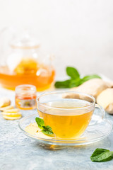 Ginger tea in a glass cup with lemon and mint on light background