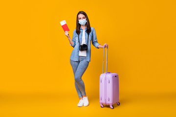 Full size photo of young lady journalist rolling bag photographer travel abroad airport quarantine registration tickets wear facial mask casual clothes isolated yellow color background
