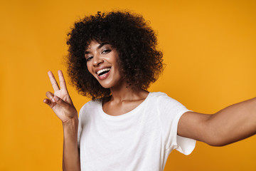Image of african american girl gesturing peace sign and taking selfie