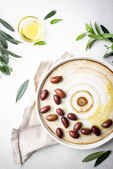 Black olives and olive oil in plate on white background, top view