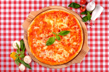 Neapolitan Margherita pizza with mozzarella cheese, basil, vegetable and tomatoes sauce, served on a wooden board for a dinner in italian restaurant background, top view. Italy food.