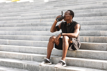 Thursty Black Male Athlete Drinking Water, Resting On Urban Stairs After Training Outdoors