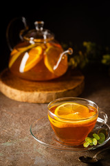 Glass teapot with hot citrus tea from oranges, lemons and limes, healthy drink on dark background