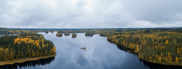 Aerial panoramic view of a beautiful lake in the forest with colorful trees during fall season. Cloudy autumn day. Finland.