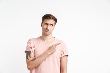 Image of displeased young man in basic t-shirt pointing finger aside