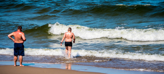 Fat father watching fat son enter the sea