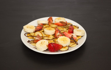 Mini pancakes on a white plate on a black background. Banana and strawberry slices. delicious and healthy Breakfast.