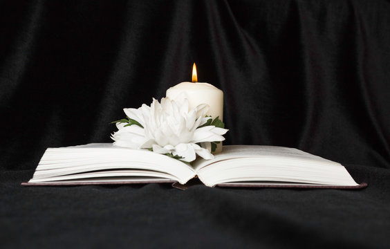 Condolence Card. A White Memorial Candle With White Flowers And An Open Book. The Funeral, The Sadness.