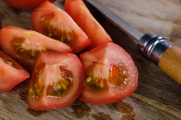 Saftige rote Tomatenstücke und ein Messer auf einem Holzbrettchen
