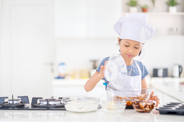 Little girl pouring flour into a bowl in kitchen