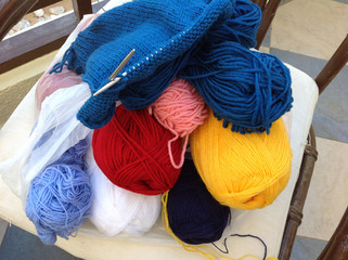 A hobby while on vacation. Needlework - knitting from blue thick yarn on spokes lies on multicolored strands of yarn