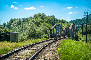 Fototapeta premium Railway bridge over river in Polish mountain. Heavy rusty steel old industrial train overpass in natural scenic landscape, blue summer sky.