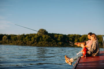 Young family fishing on the pier on the river or lake in summertime. Photography for ad or blog about family and travel