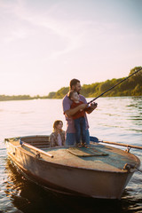 Fototapeta na wymiar Happy family fishing on boat on river in summertime. Father teaches son fishing. Photo for blog about family travel