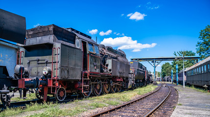 Naklejka premium Ogromna zabytkowa lokomotywa parowa, szczegółowo malowane stalowe koła na czerwono. Parowóz napędzany węglem stoi na bocznicy. Klasyczne gigantyczne ciężkie maszyny kolejowe. Widok z boku na części mocy maszyny.