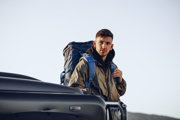 Naklejka premium Portrait of a young traveler man in hiking equipment standing near his off-road car