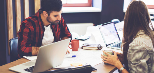 Crew of young male and female trainees of architect company brainstorming working on graphic outlays discussing details in planning using laptop computers and free internet connection in campus