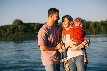 Young family hug each other on river background. Summer photography for blog or advertising about...