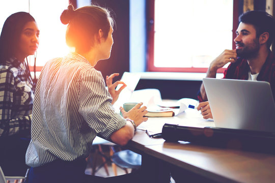 Young skilled female journalists explaining her concept of writing popular articles for social networks during working meeting with editor and colleague in coworking office with wifi zone and gadgets