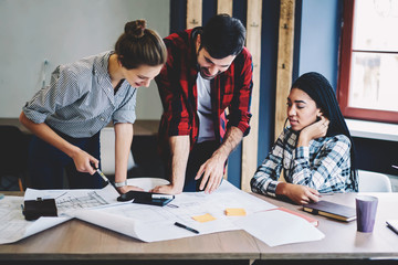 Crew of creative male and female designers dressed in casual clothes working on making sketch of exterior and interior cooperating while brainstorming drawing graphic standing near desk in coworking