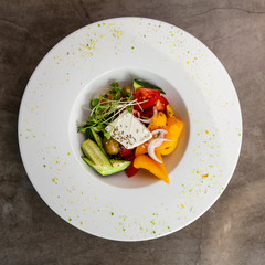 Greek salad in white plate on grey table.