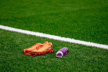 Football boots with bottle of water on green grass or pitch