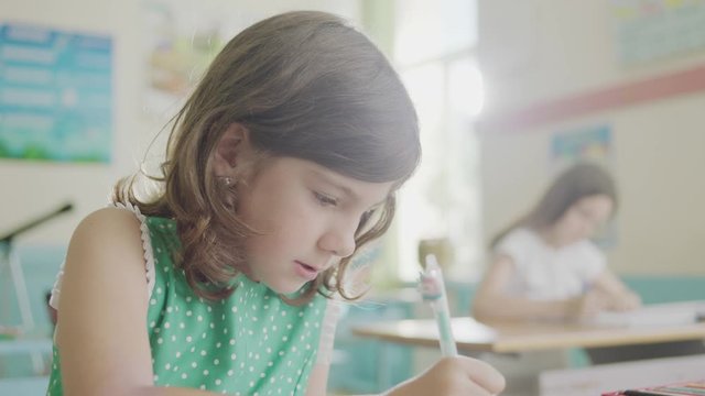 A girl student writing in an exercise notebook in a classroom of an elementary school.
