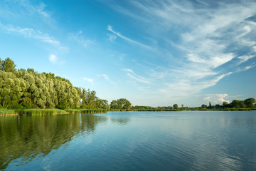 Fototapeta na wymiar Cirrus clouds in the blue sky over a lake and a green forest, Stankow, Poland